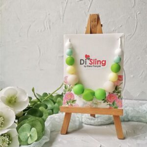 Colar mordedor Disling em silicone verde e tons pastel, exposto num mini cavalete de madeira. As contas arredondadas oferecem textura segura para o bebé. O fundo neutro realça as cores suaves do acessório.