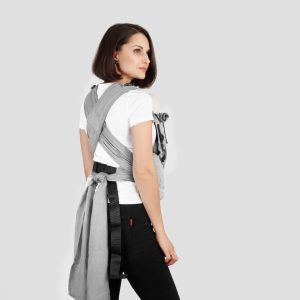 A imagem apresenta uma mochila ergonómica em tons de cinza, com alças acolchoadas e sistema de ajuste na cintura. O tecido é suave e resistente, proporcionando conforto tanto para o adulto como para o bebé. O bebé é transportado na frente ou nas costas, permitindo uma postura natural e segura durante o uso.