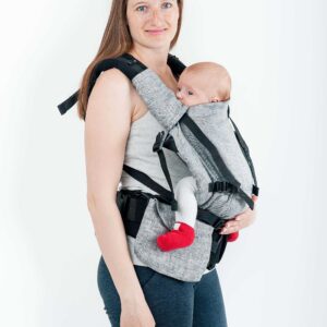 A imagem mostra uma mochila ergonómica em tons de cinza, com alças acolchoadas e fechos ajustáveis. O bebé está posicionado na frente do adulto, com uma postura confortável e segura. O contexto sugere uma utilização prática para passeios ou atividades diárias.